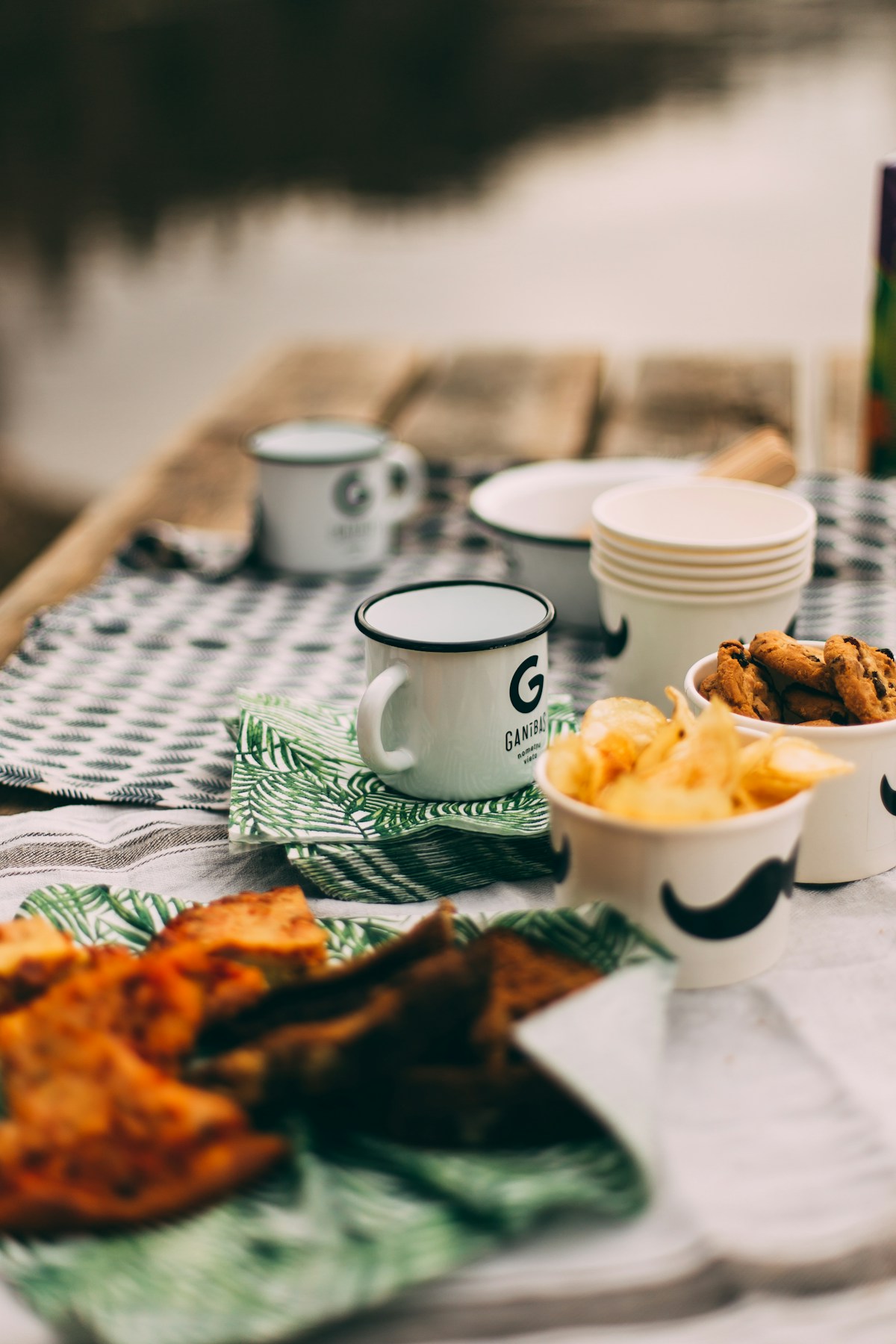 Enamel mugs and a picnic spread on a camp table